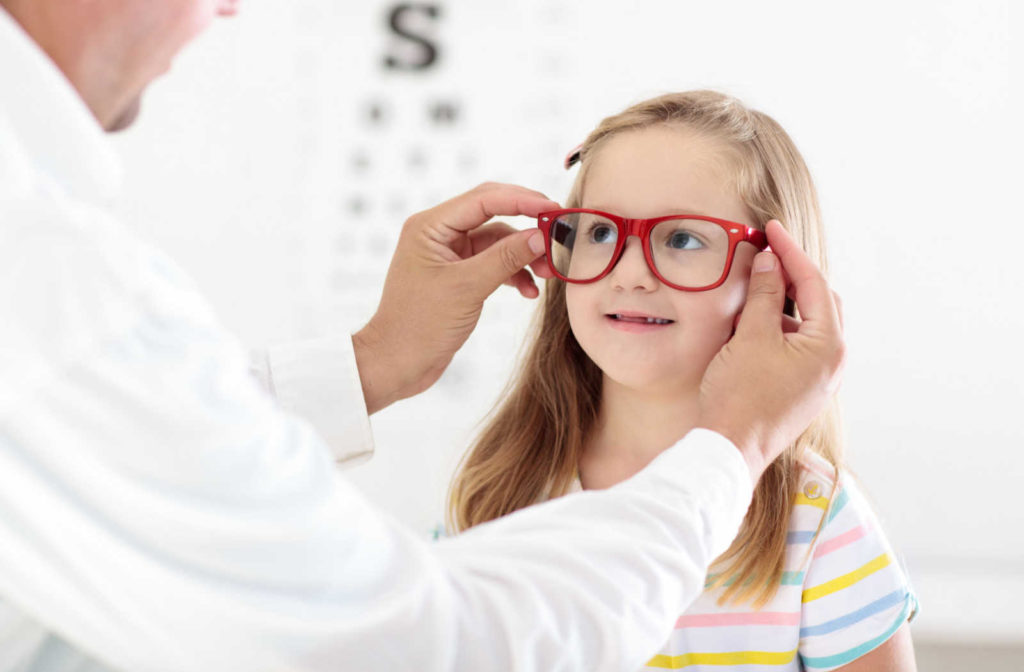 A male eye doctor is fitting new red eyeglasses for his preschooler female patient.