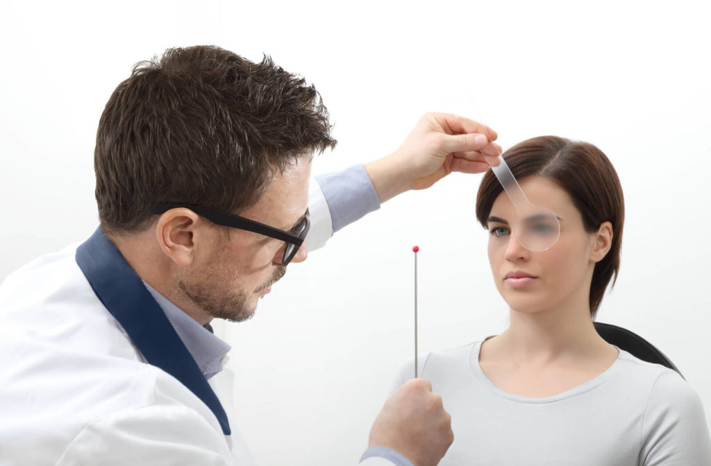 A male optician is holding a stick with a red small ball at the tip and moving it while the female patients try to follow the movement.