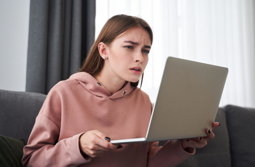 A teenager is squinting her eyes and she's looking to close on the screen while using a laptop computer.