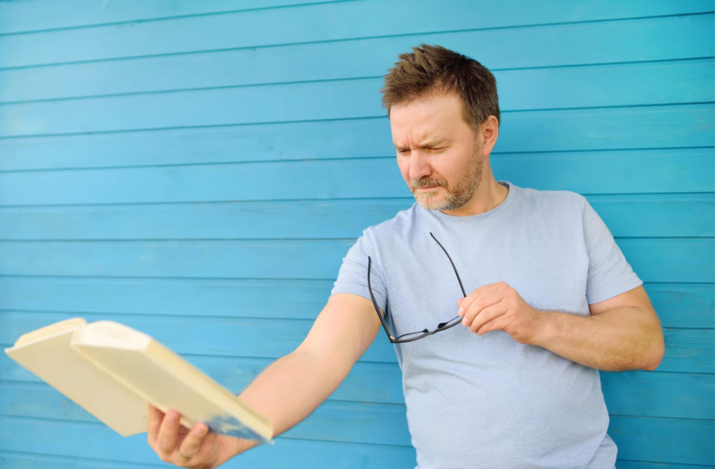 A mature man is reading a book and holding it far from him.