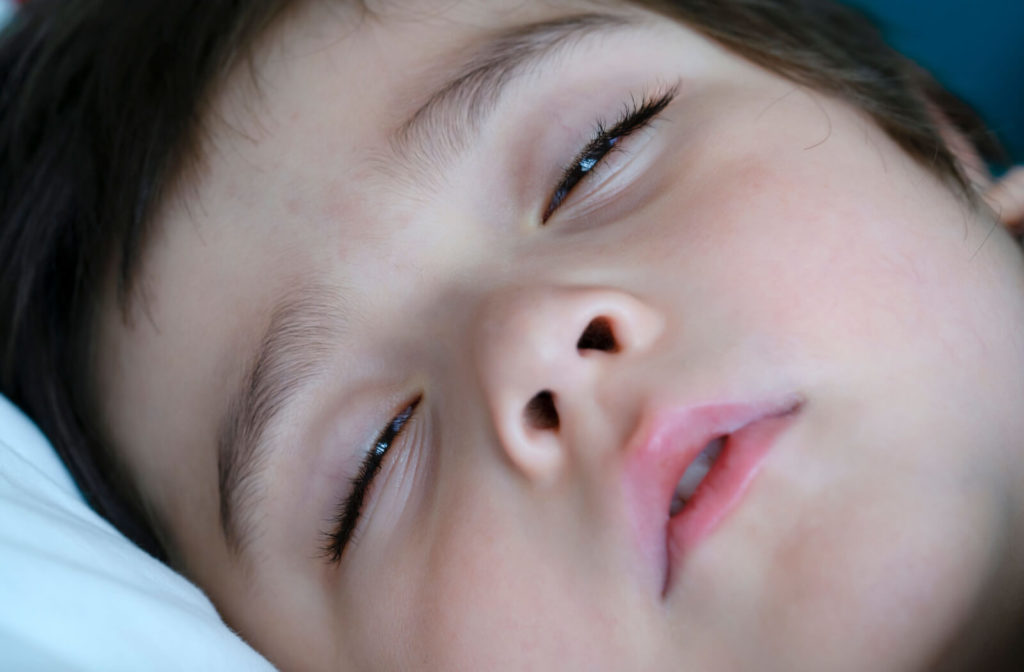 A close-up of a boy sleeping with his eyes half open.
