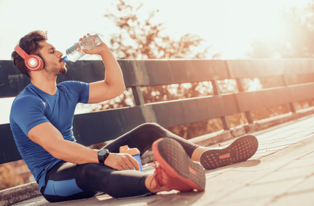 A fit bearded man with his headphones on drinking a bottle of water after exercising.