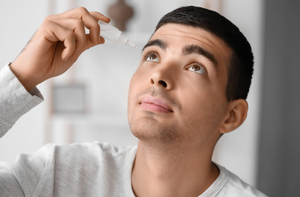 A young man using artificial tears to help him remove his contact lens safely.