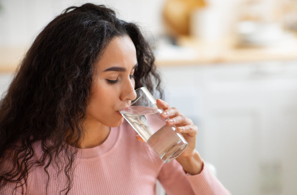 A woman in a pink sweater drinking a glass of water.