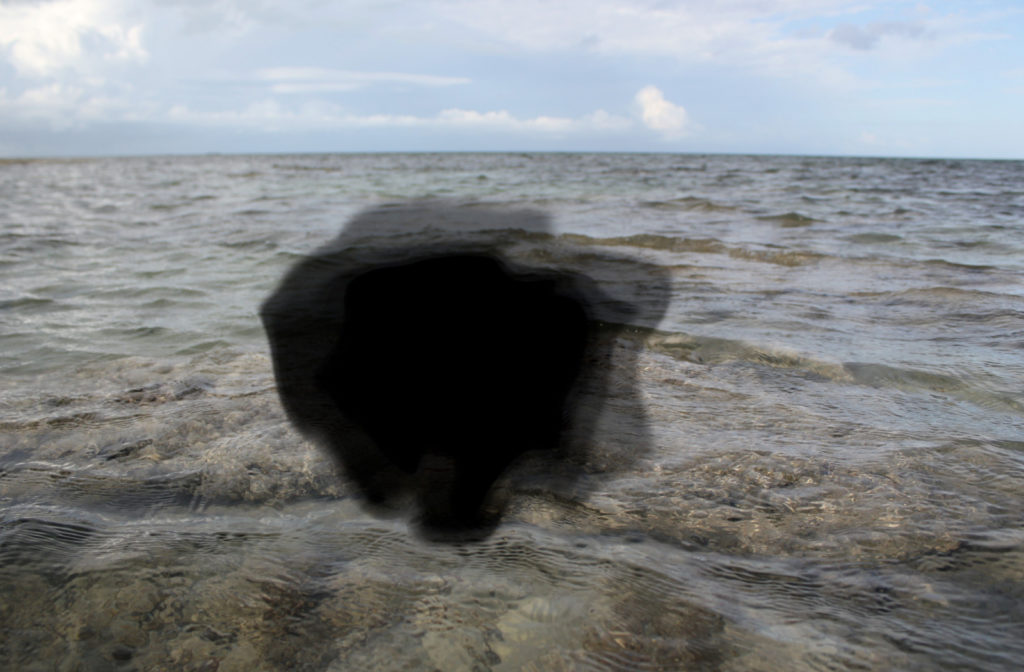 A point of view of a person with age-related macular degeneration looking at the ocean. There's a black spot in the middle of their vision, distorting their view of the ocean.