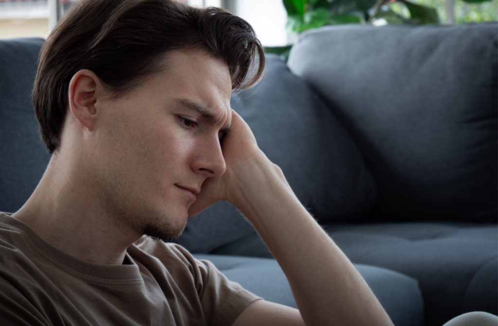 An anxious-looking young man sitting on a couch while in deep thought.