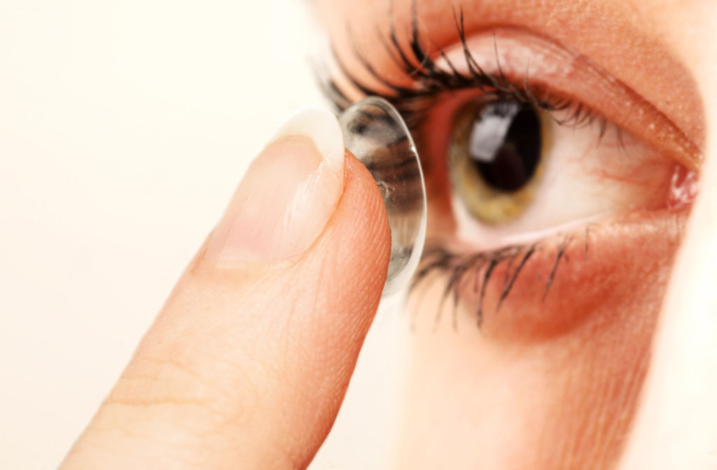 A close up of a contact lens on a finger tip being inserted into an eye.