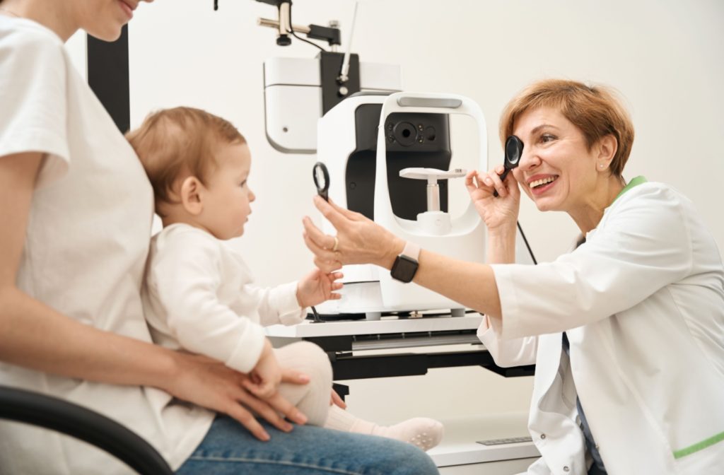 An optometrist performing an eye exam on an infant while smiling.