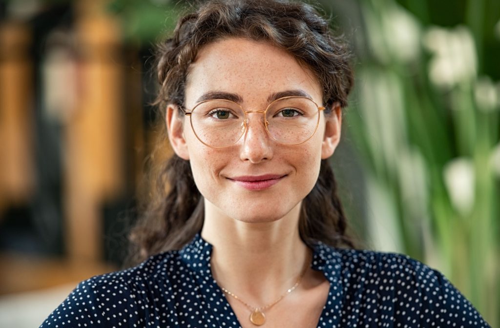 A smiling freckled woman in gold-rimmed eyeglasses looks confidently into the camera