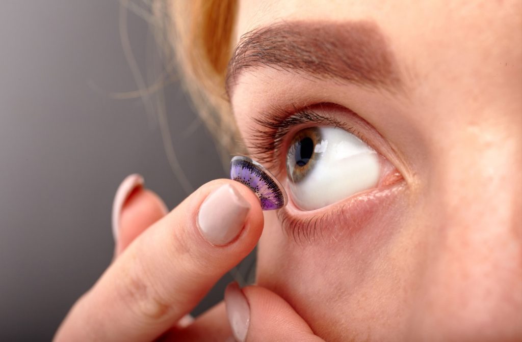 A closeup of a young woman applying her purple-colored soft contact lenses.