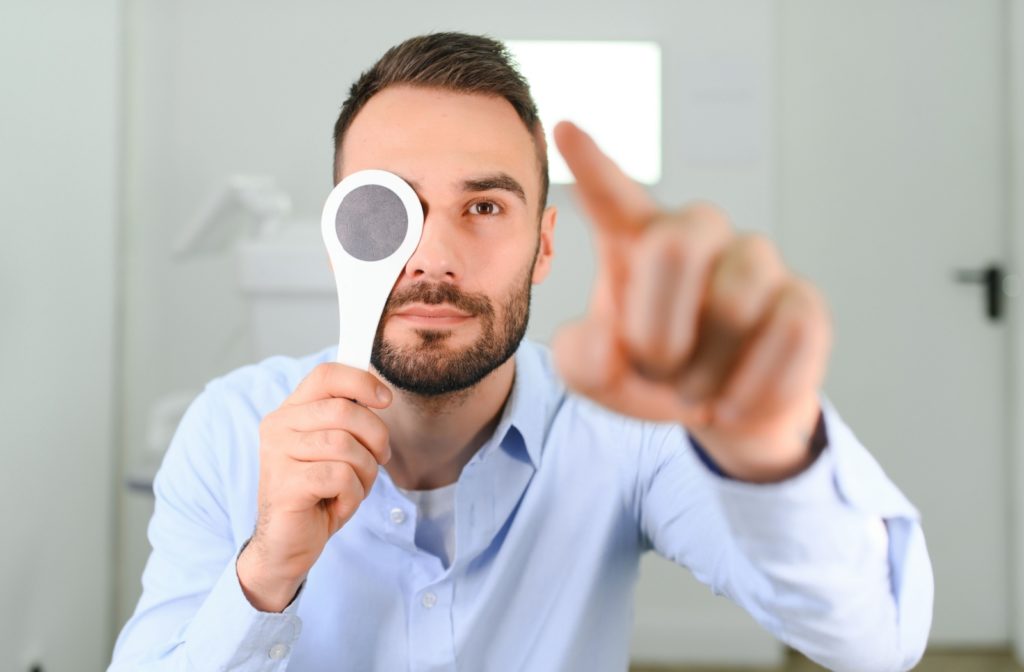 A man hold an eye cover over his right eye while testing his depth perception by looking at his left hand outstretched in front of him.