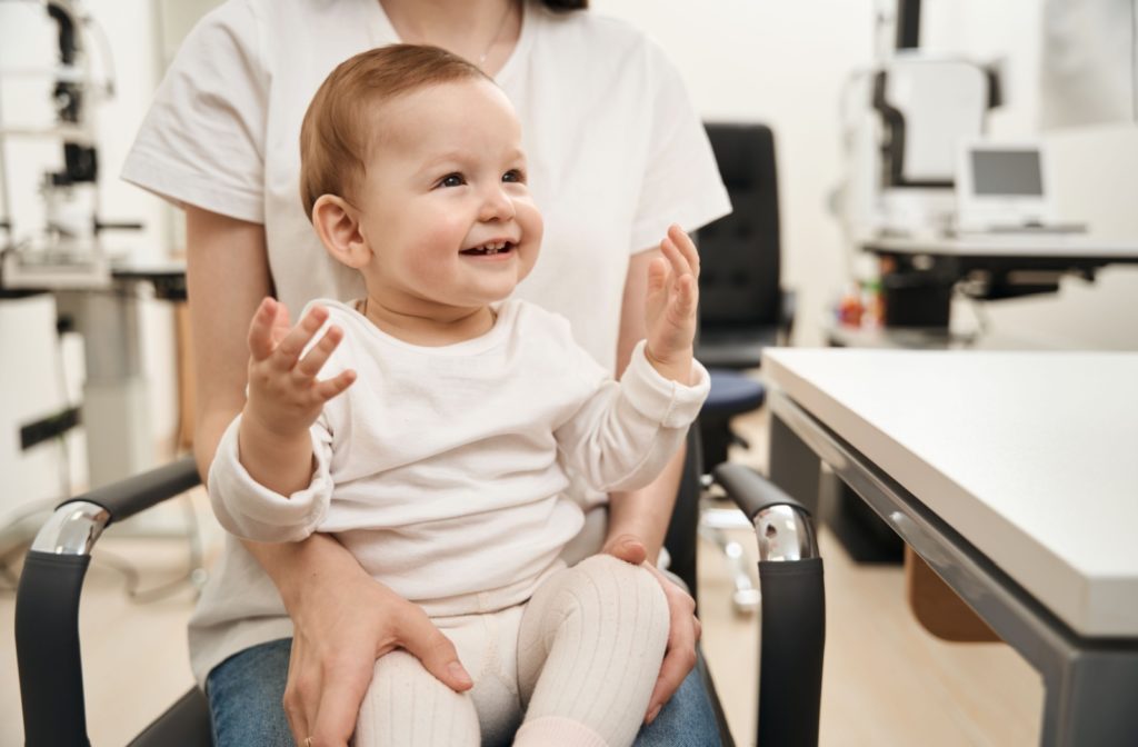 Toddler sitting happily on a parent's lap during an eye exam at the optometrist's office.