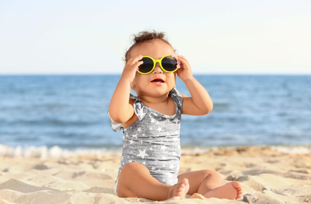 A child sitting on the sun wearing sunglasses with flowers on them to protect their eyes while spending time outdoors.