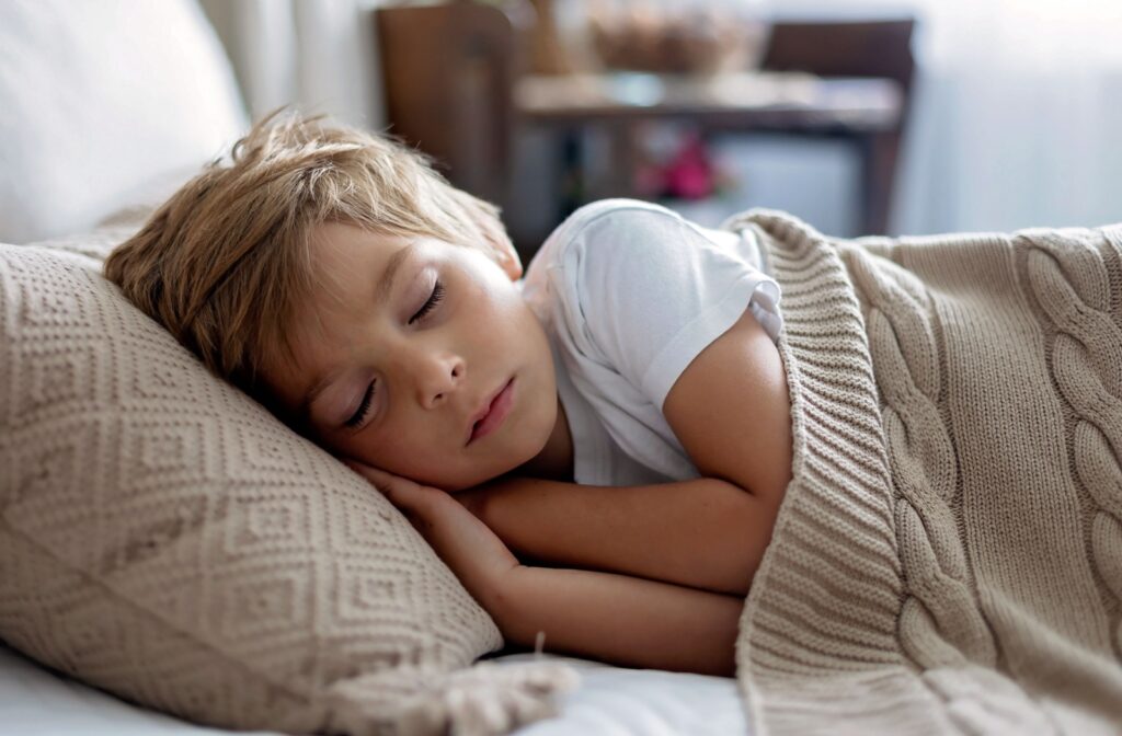 A child sleeping in bed, wearing ortho-k lenses to reshape the cornea overnight, slowing myopia progression and providing clear vision during the day.
