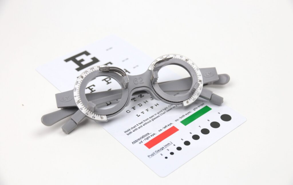 A pair of trial frames sit on top of a Snellen Eye Chart with prescription information on the bottom of the chat.