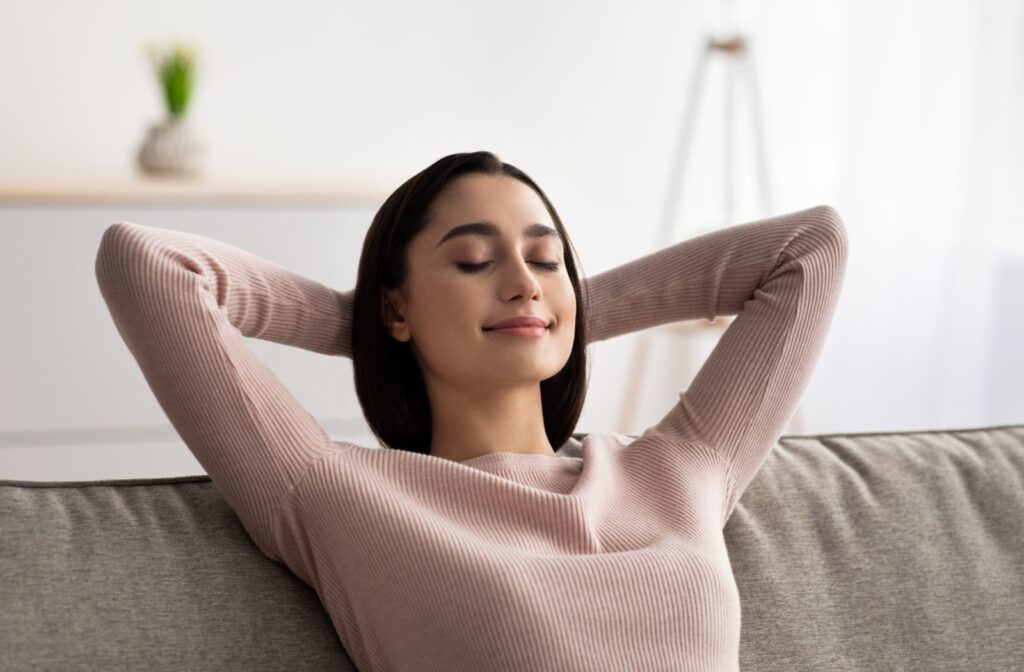 A person sitting with their hands behind their head and their eyes closed, resting their eyes.