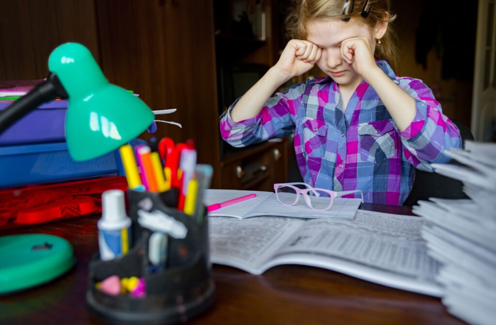 A young student rubbing their eyes while doing school work.